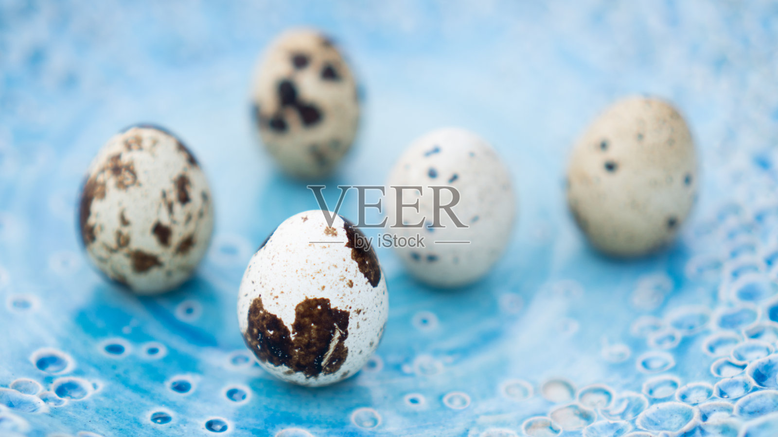 新鲜的鹌鹑蛋放在漂亮的蓝色手工盘子里。背景照片摄影图片