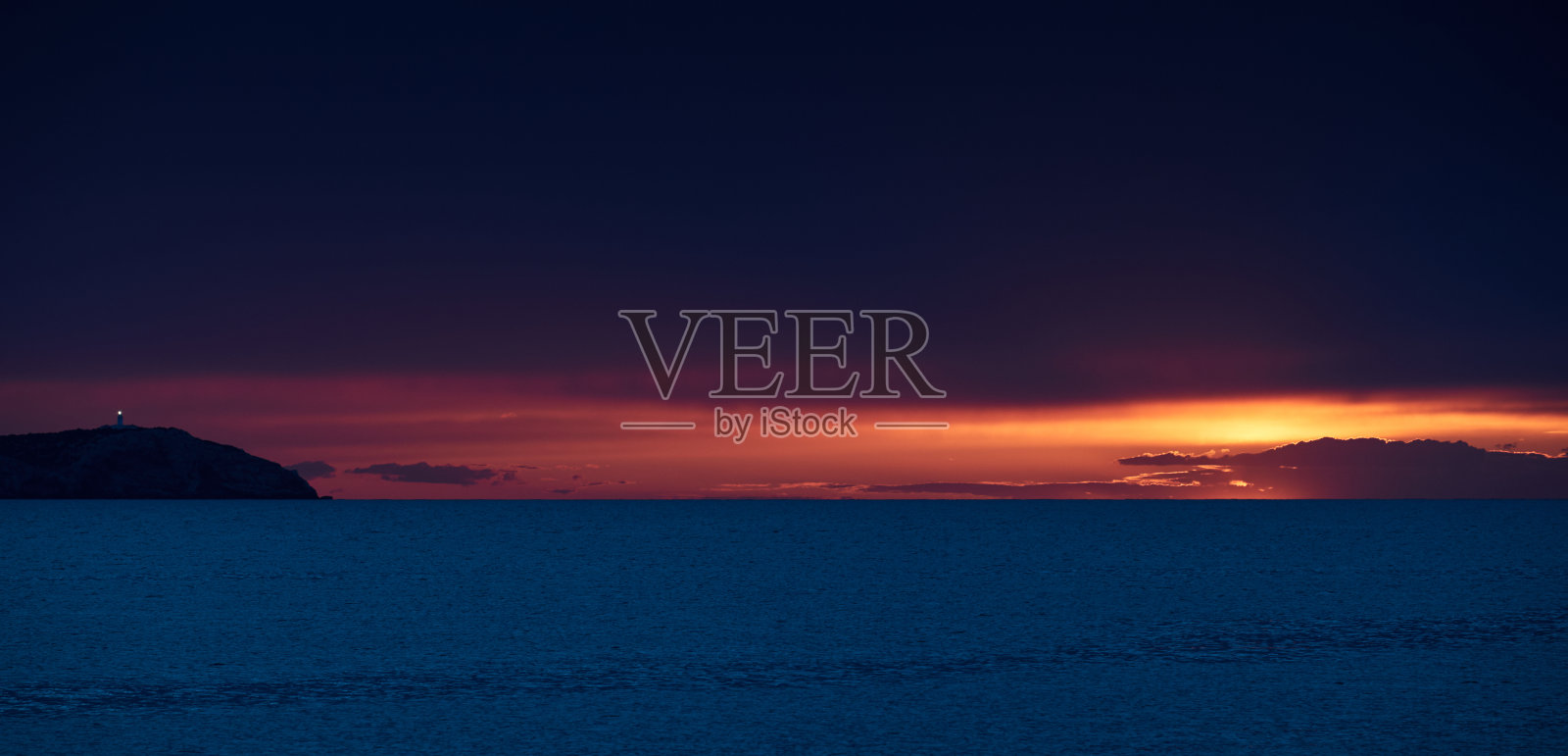 日落时山上的灯塔，橙色的天空，平静的大海，路上的阳光照片摄影图片