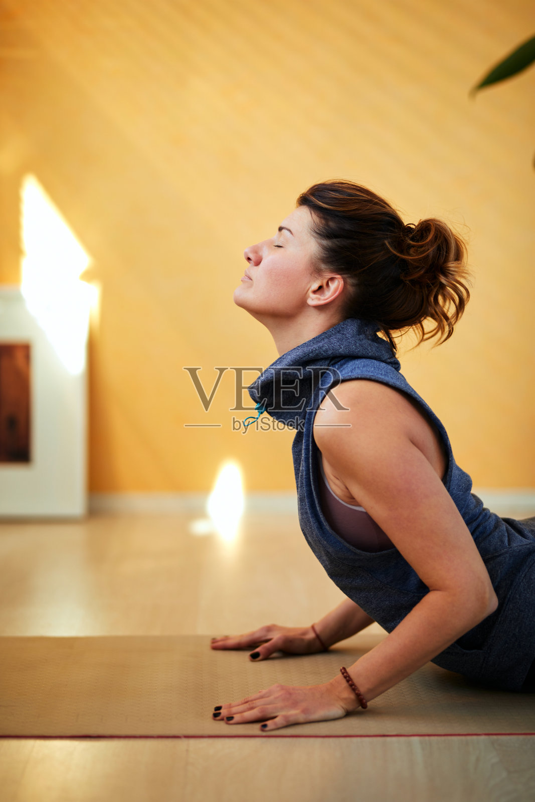 中年白人褐发女性早上躺在家里的瑜伽垫上练习瑜伽。瑜伽在家的概念。照片摄影图片