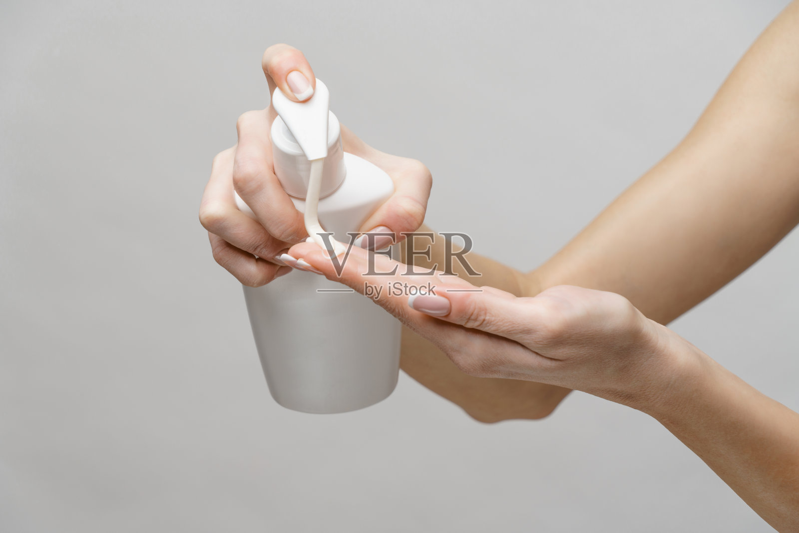 女性双手使用洗手液或肥皂液，背景为浅灰色照片摄影图片