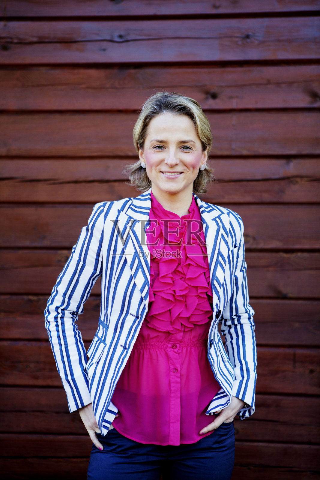 非常漂亮的年轻女子，穿着红色优雅的上衣和白色条纹的正装夹克，双手插在口袋里，面带微笑，充满自信和放松照片摄影图片