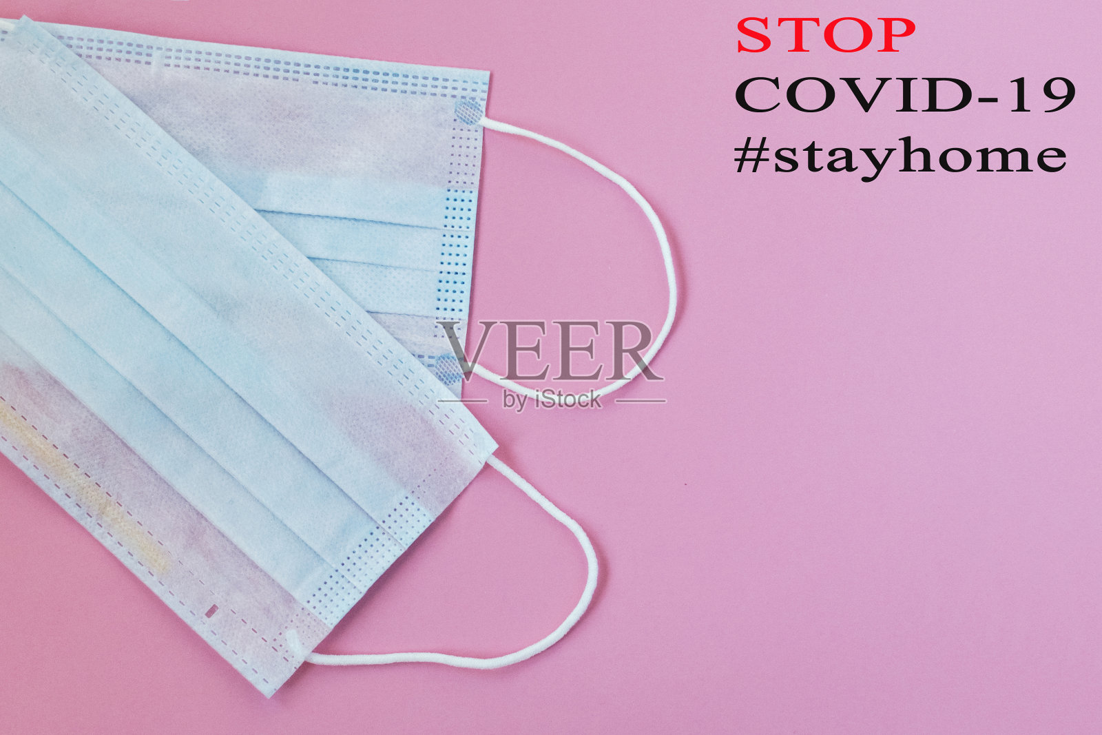 粉色背景的蓝色医用口罩，标签为“停止，2019冠状病毒病，#待在家里”。Covid-19 -新冠肺炎。呼吸防护口罩。大流行。照片摄影图片