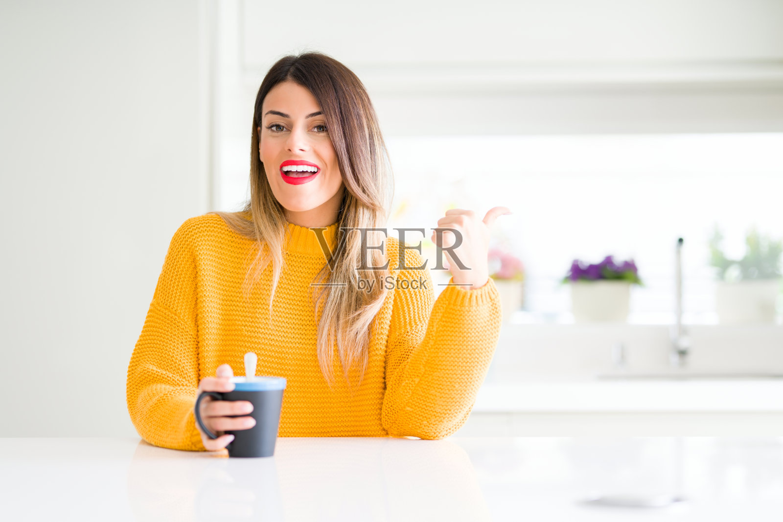 年轻美丽的女人喝一杯咖啡在家指指点点，并显示与拇指向上的一边与幸福的脸微笑照片摄影图片