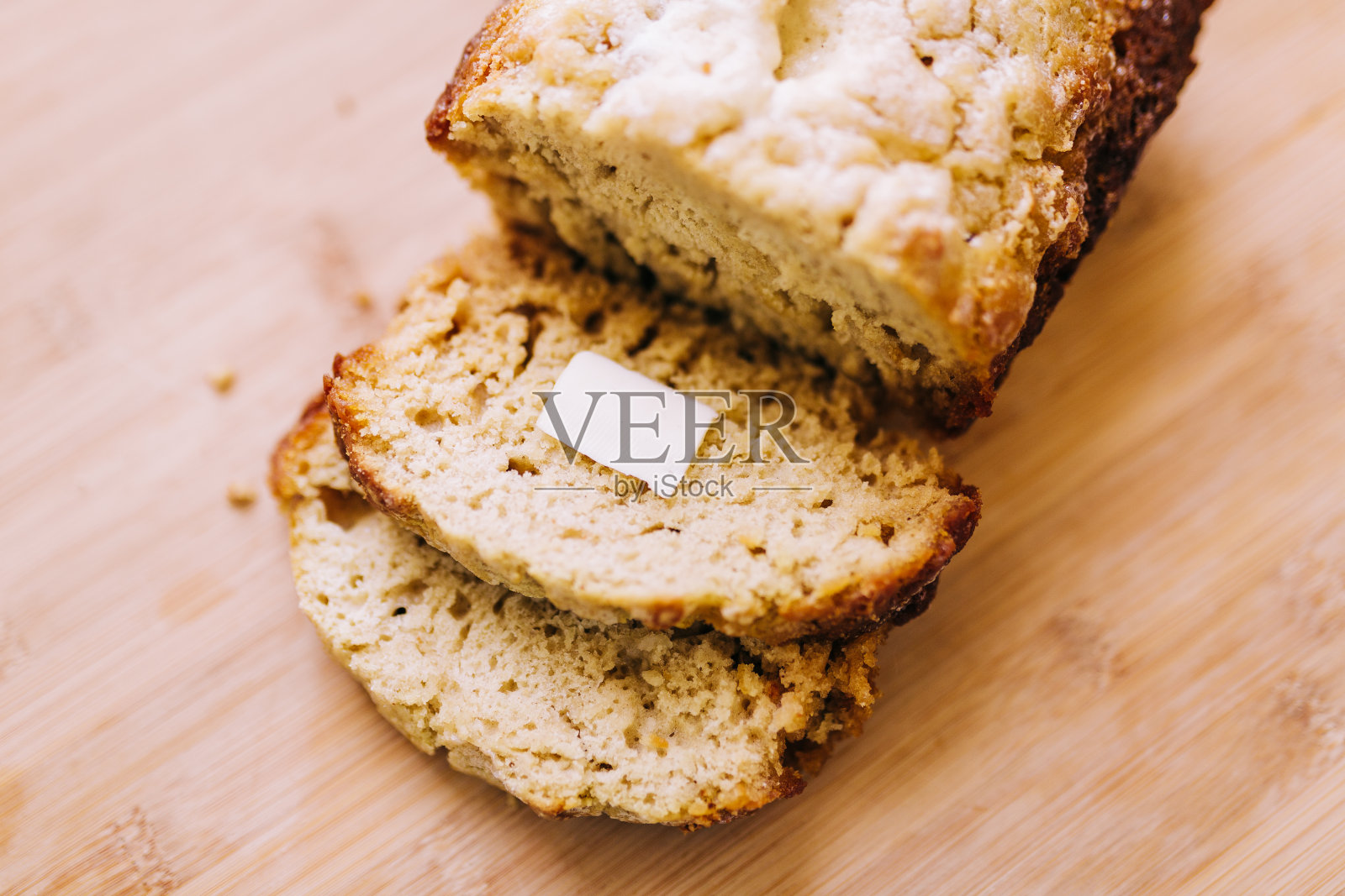 木头表面上的一块硬皮啤酒面包，面包片上涂着黄油。照片摄影图片