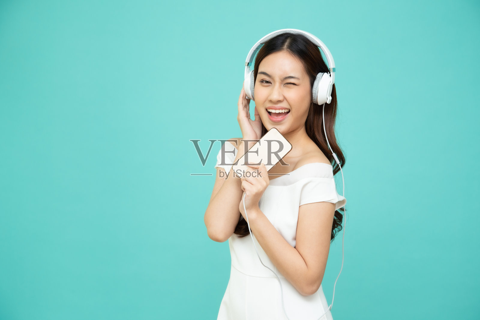 年轻的亚洲美女听音乐耳机在智能手机上播放列表歌曲应用隔离在绿色背景照片摄影图片