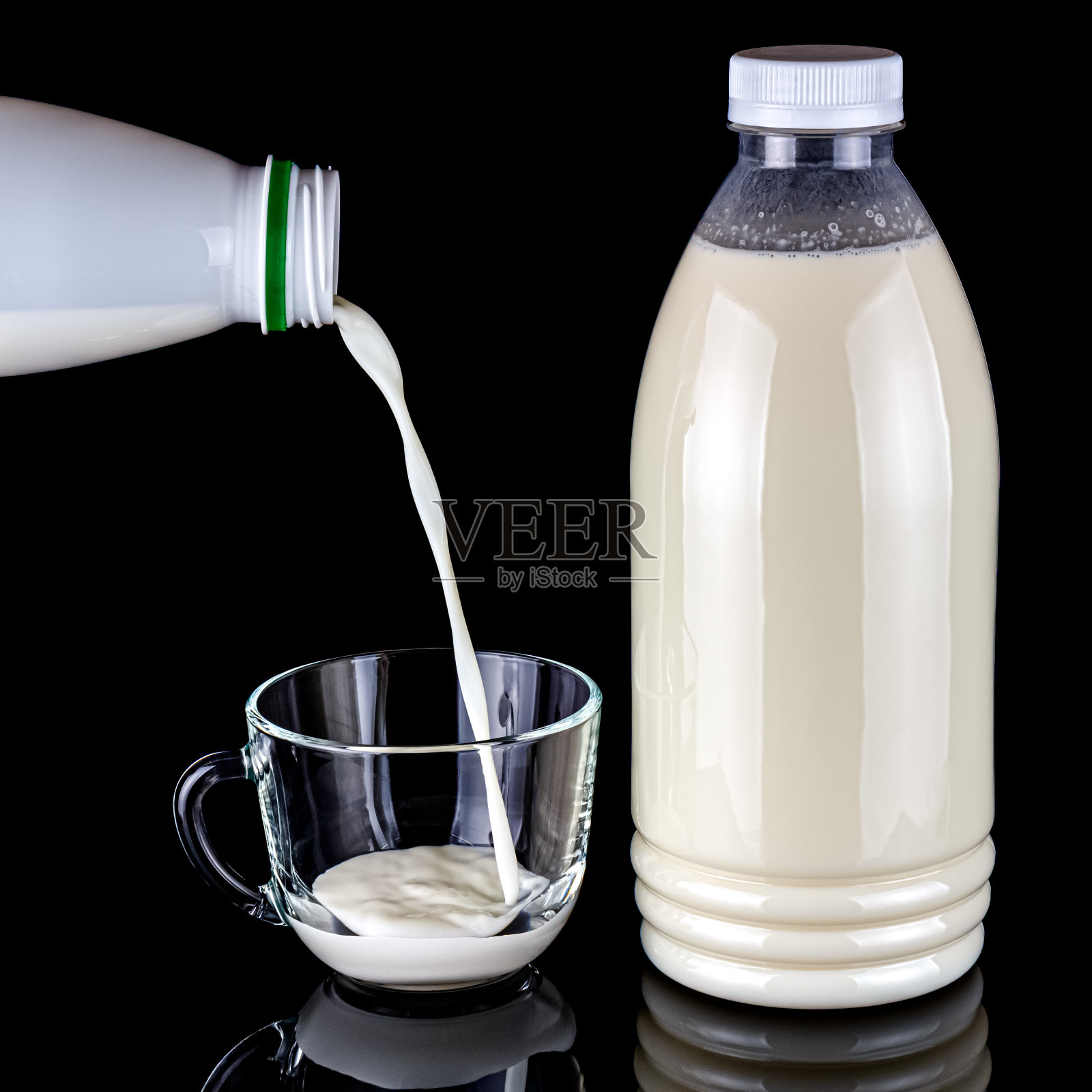 将牛奶从白色塑料瓶倒入透明的玻璃杯中，牛奶被隔离在黑色的背景上，在光滑的表面上反射照片摄影图片