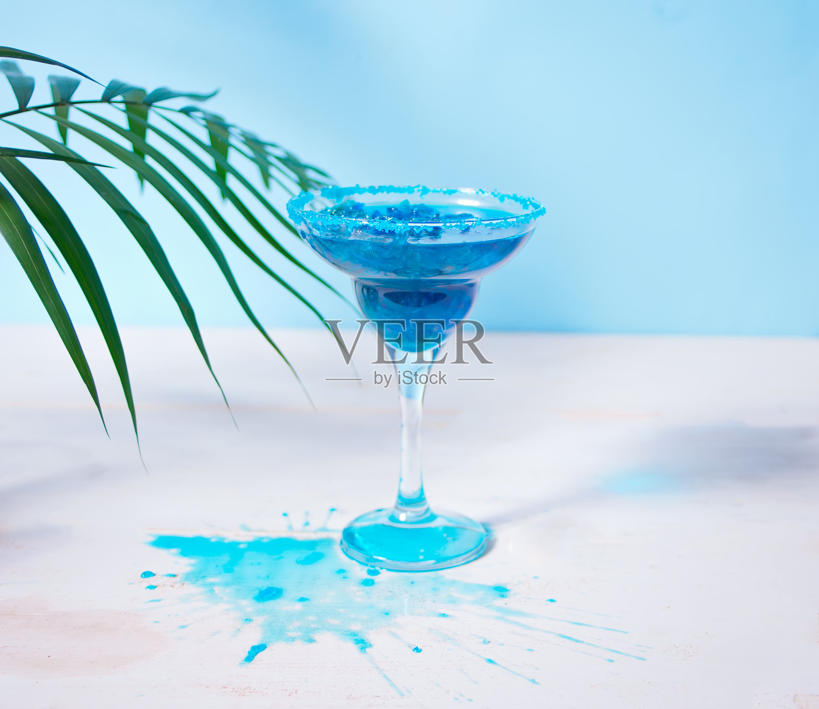 一杯棕榈叶下的蓝色鸡尾酒。夏威夷鸡尾酒，泻湖鸡尾酒，库拉索岛。照片摄影图片