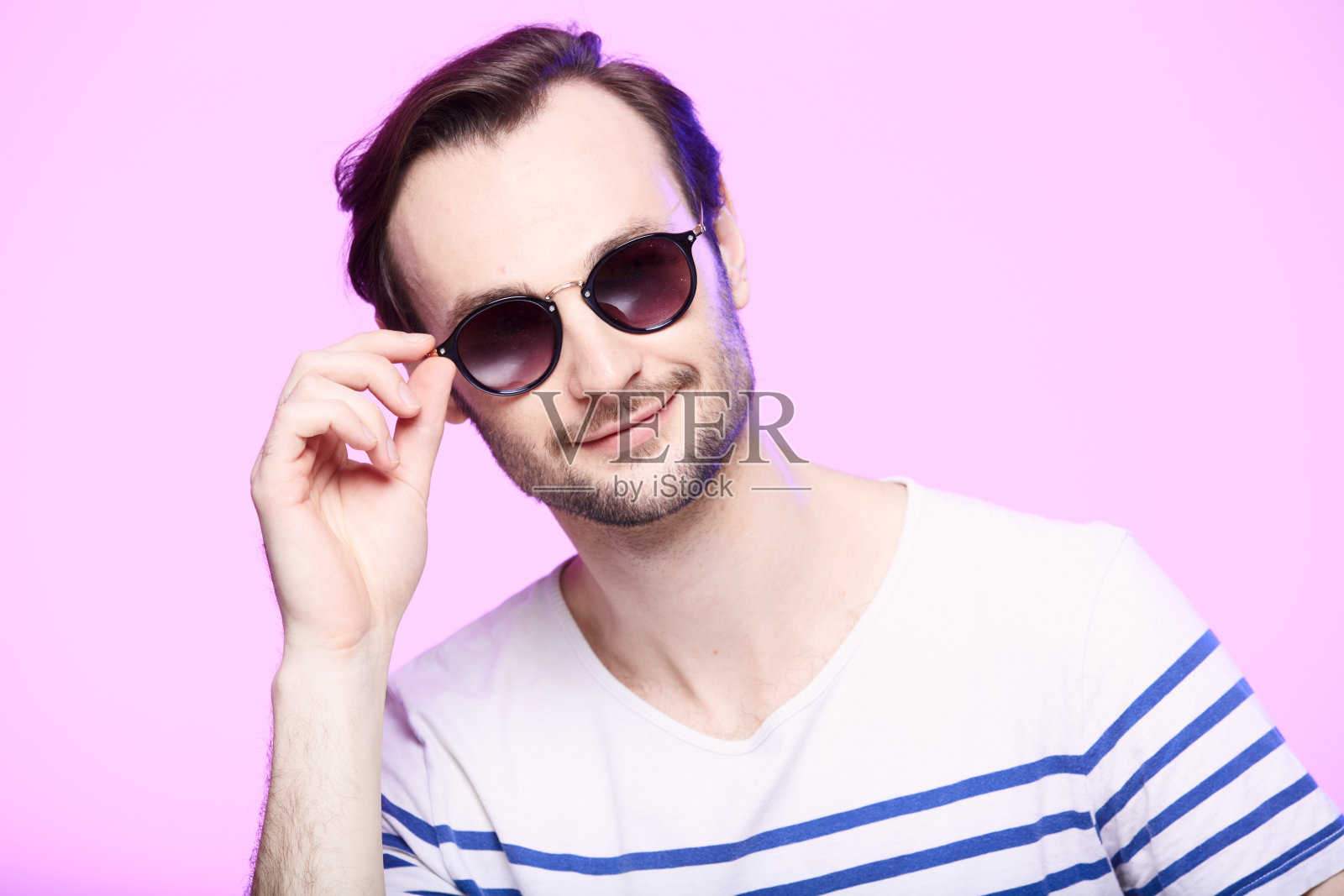 工作室拍摄的英俊男子戴着太阳镜在粉红色的背景。照片摄影图片