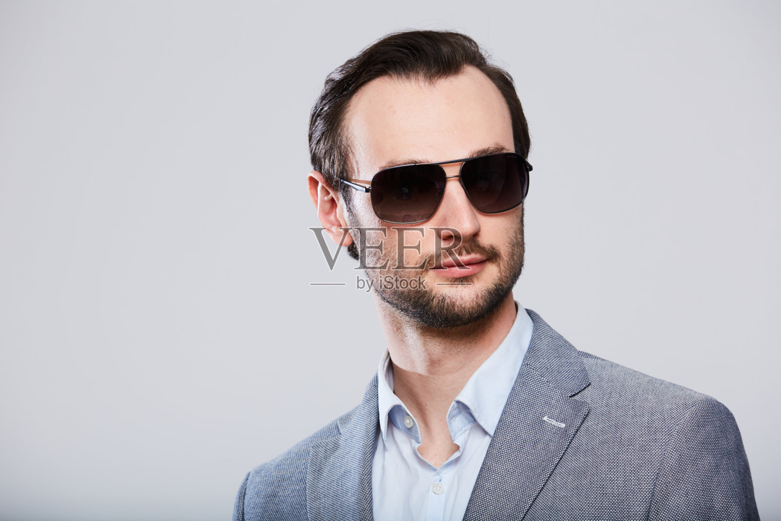 优雅的年轻英俊的男人戴着太阳镜，穿着时髦的灰色夹克。工作室时尚肖像。照片摄影图片