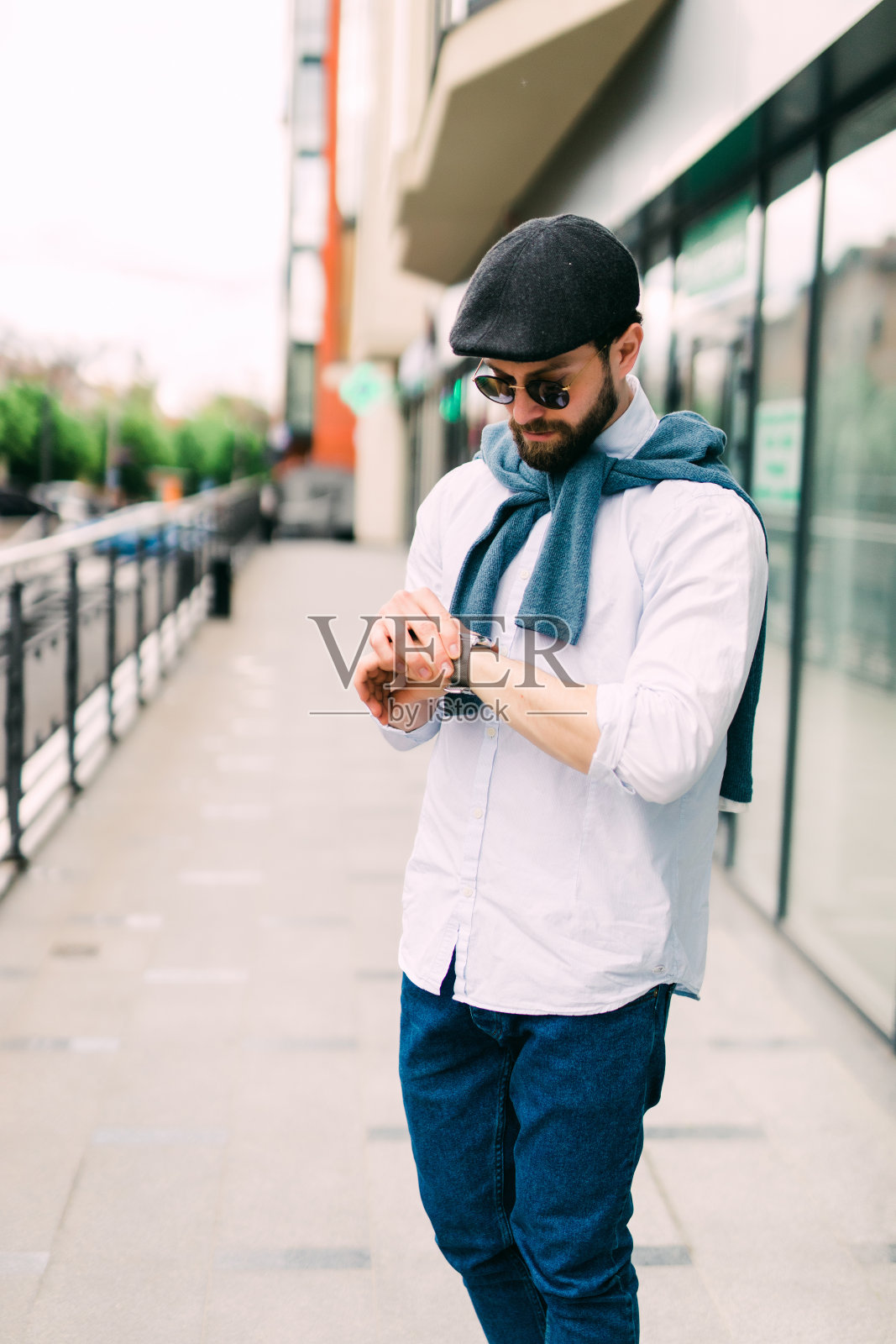 我应该能及时赶到。一个自信的年轻人站在户外，看着他的手表，背景是城市风景照片摄影图片