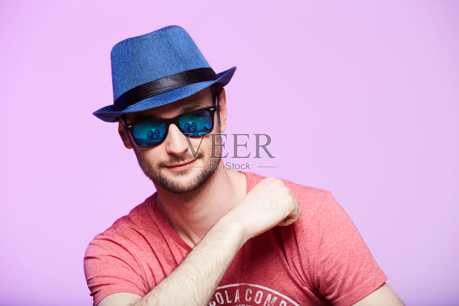 戴着蓝色帽子的年轻潮男。工作室拍摄在粉红色的背景。照片摄影图片