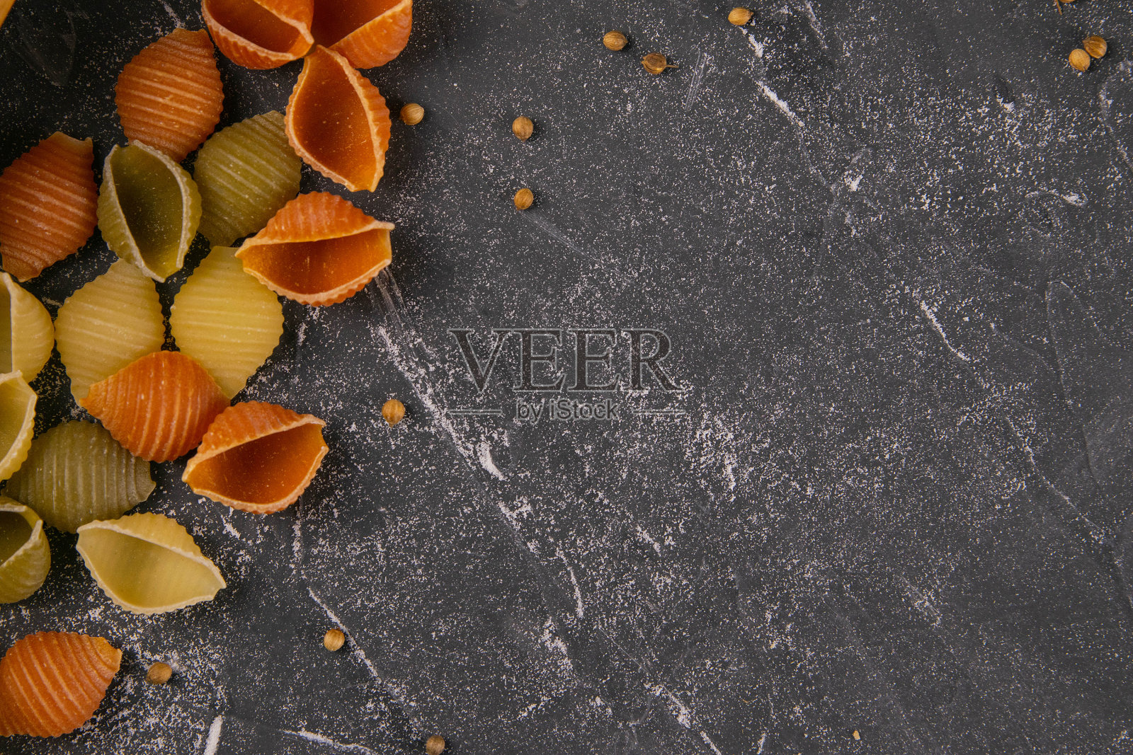 意大利面食Conchiglie Rigate，混合了五颜六色的生壳散落在桌子上，留下了一片空白。质感的意大利食物背景概念。俯视图平放近照片摄影图片