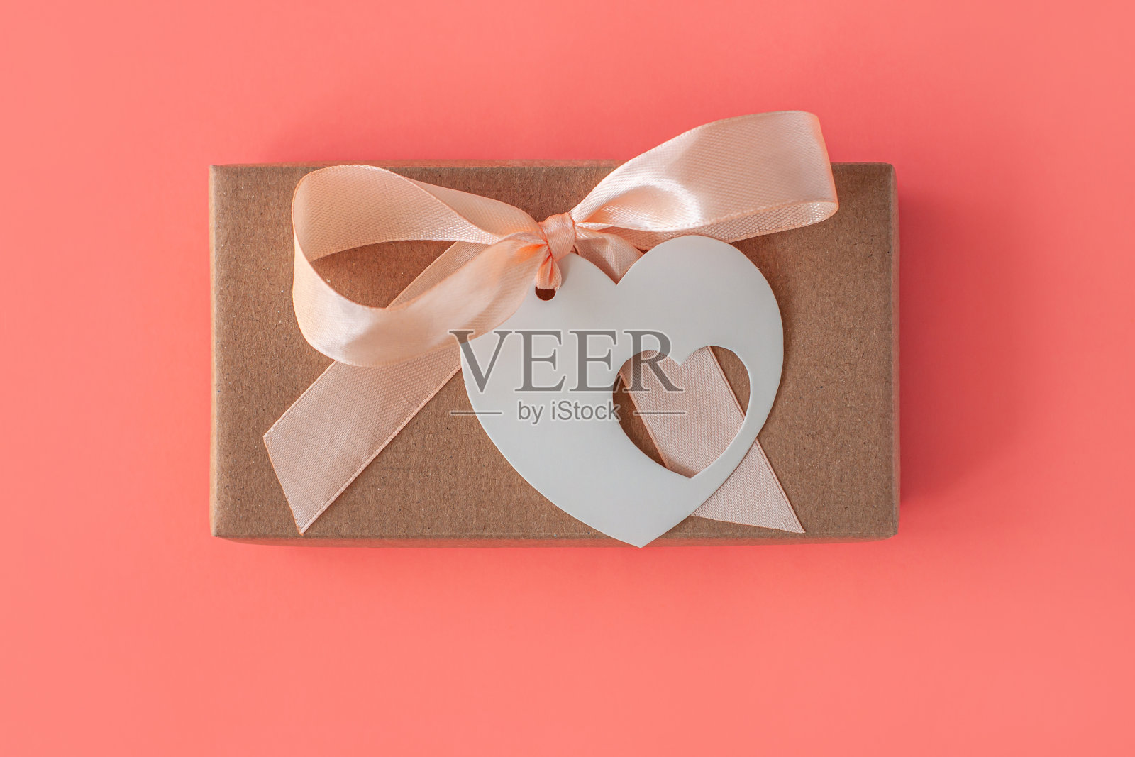棕色牛皮纸礼盒丝带蝴蝶结和心形卡片标签在粉红色珊瑚的背景。假日包装平铺。照片摄影图片