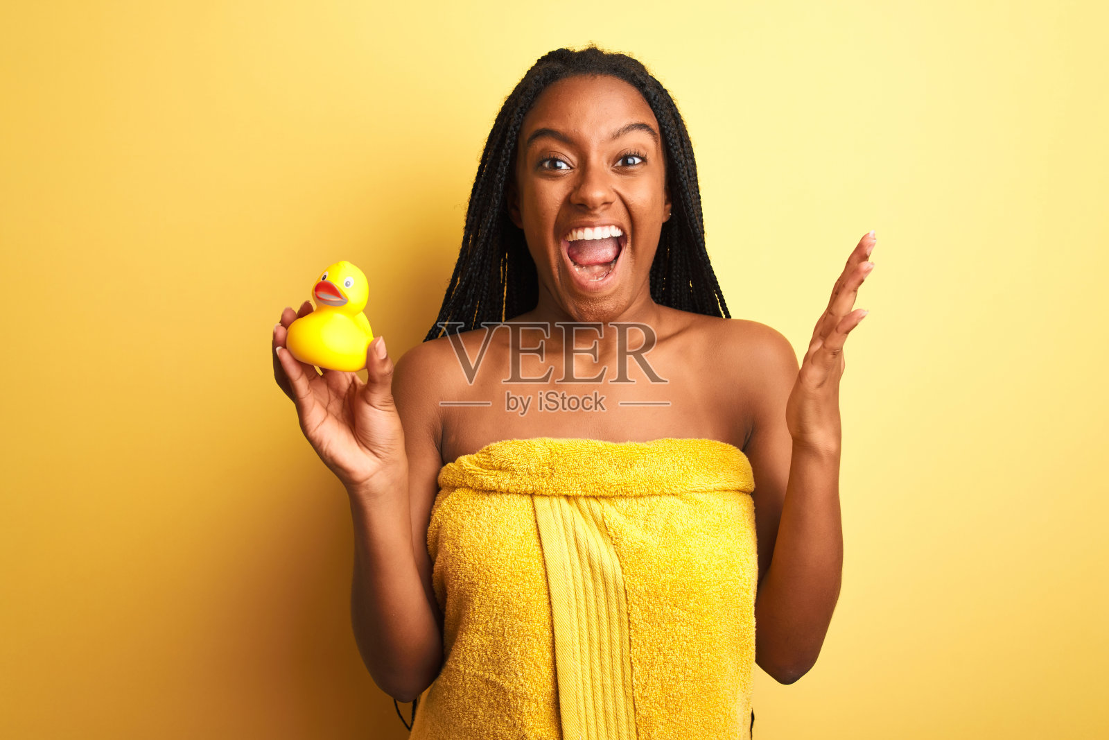 非裔美国妇女穿着浴巾抱着玩具鸭子越过孤立的黄色背景非常高兴和兴奋，胜利者的表情庆祝胜利尖叫着大大的微笑和举起手照片摄影图片