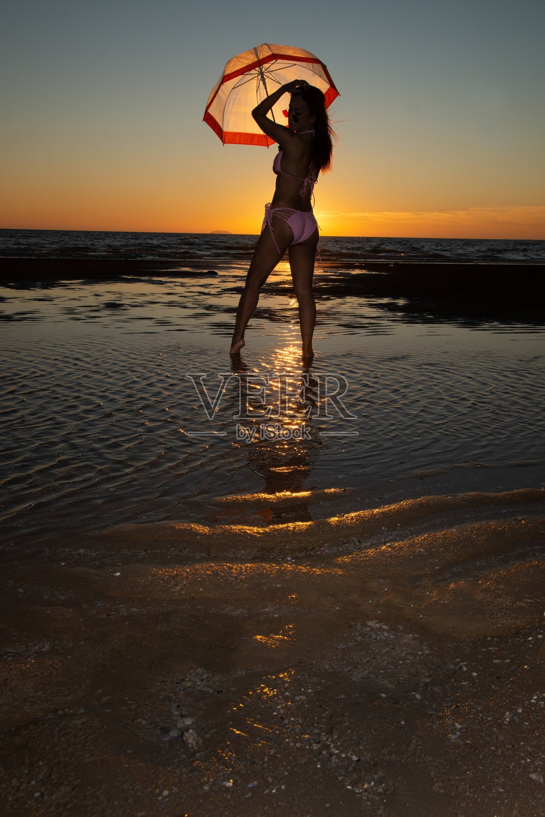 身穿泳衣、打着伞站在海滩上的年长亚洲女性剪影照片摄影图片