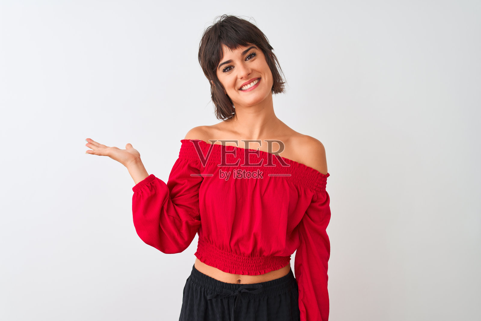 年轻美丽的女人穿着红色的夏季t恤站在孤立的白色背景微笑着提出和指向与手掌看着相机。照片摄影图片