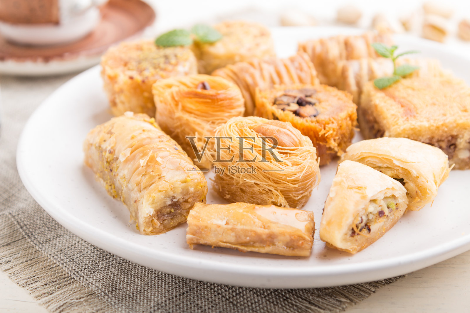 传统的阿拉伯甜点(kunafa, baklava)和一杯咖啡，在白色的木质背景和亚麻织物上。侧视图，特写，选择性聚焦。照片摄影图片