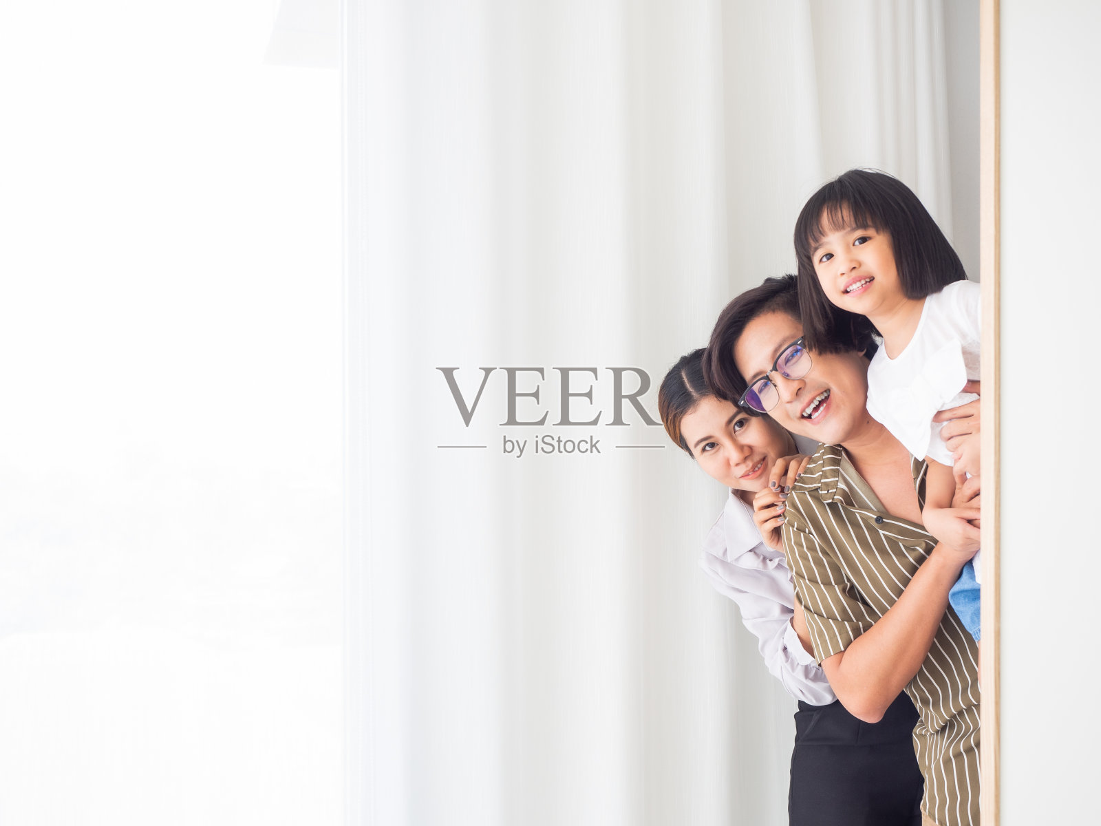 幸福家庭在卧室的概念。爸爸、妈妈和女儿在壁橱后面玩捉迷藏。童年、乐趣、欢乐、游戏和幸福概念复制空间。照片摄影图片