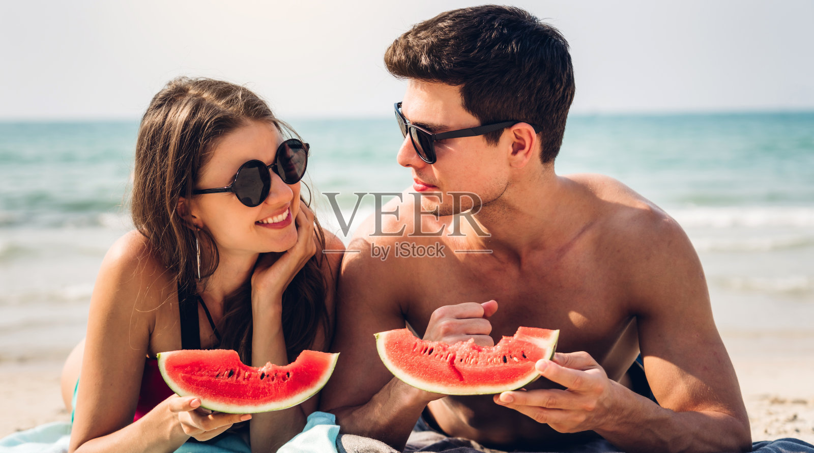 浪漫的情侣，年轻的情侣们在热带海滩上放松地抱着吃着一片西瓜。暑假照片摄影图片