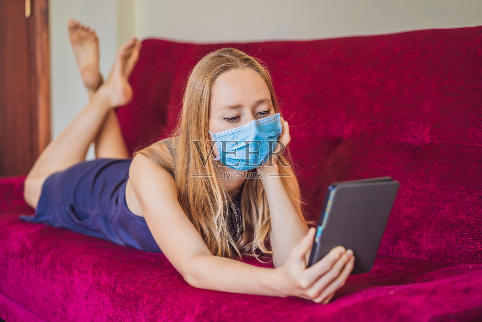戴口罩的女人在沙发上看书。居家隔离。呆在家里。新冠病毒照片摄影图片