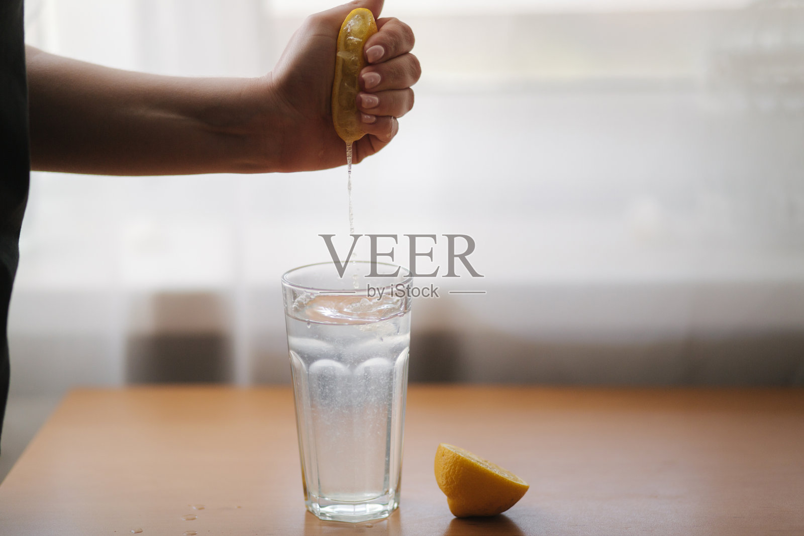 女人用手挤柠檬汁在玻璃杯里加水。和柠檬水。新鲜饮品检疫照片摄影图片