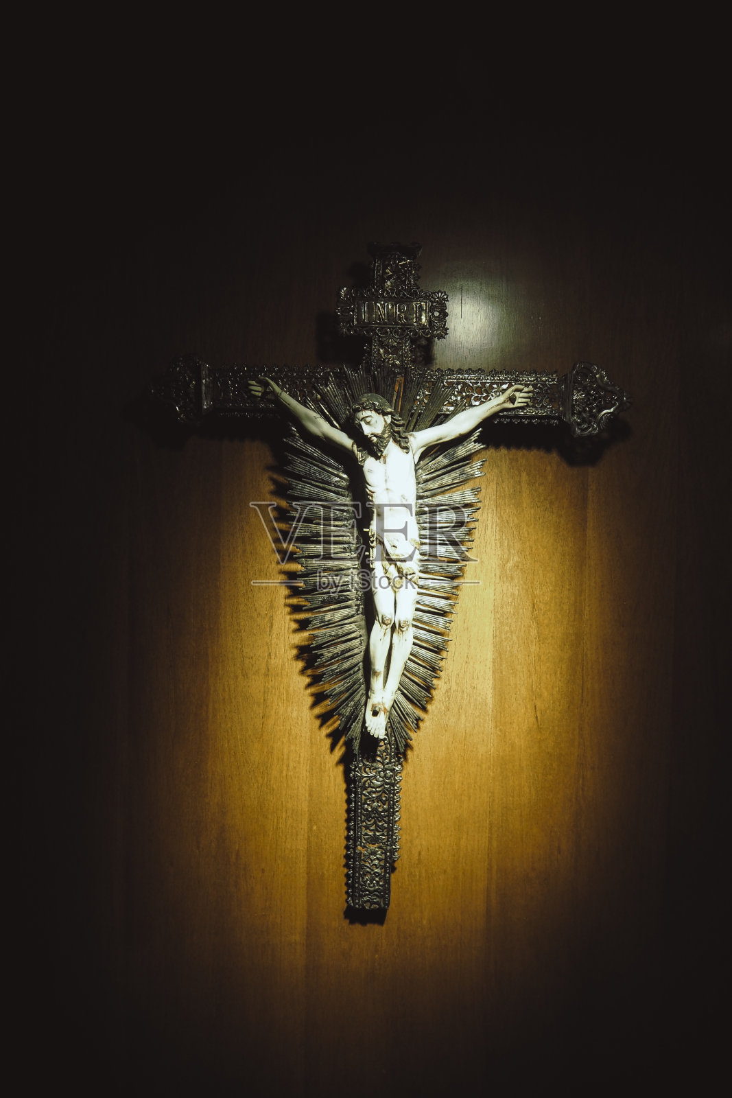 耶稣的十字架吊坠挂在棕色的木墙上，用聚光灯照射到十字架上照片摄影图片