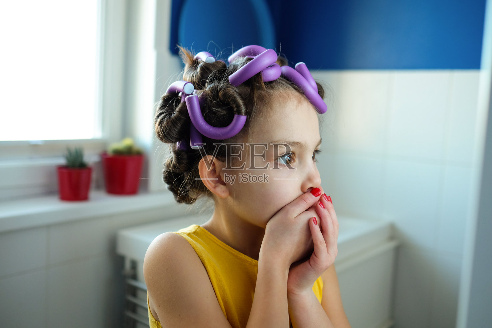 一个小女孩假装成人，或者她的妈妈在她的头发卷看着镜子。孩子们假装成大人的概念。照片摄影图片