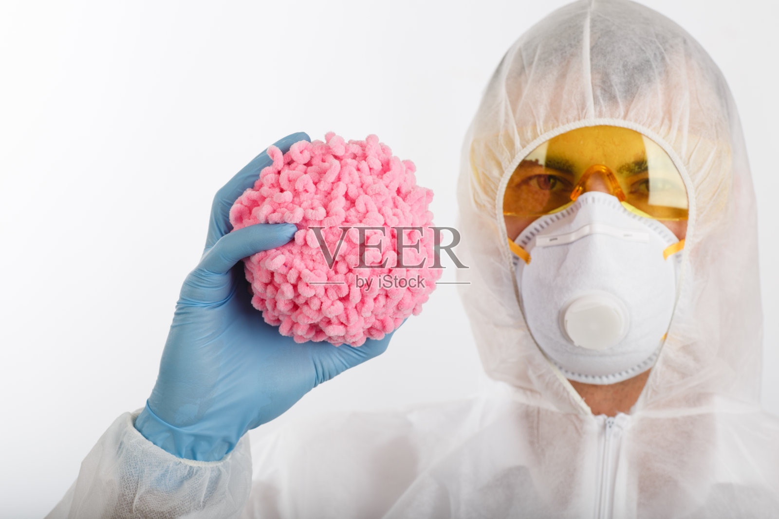 身穿防疫服的医生拿着粉色球状物，类似冠状病毒照片摄影图片