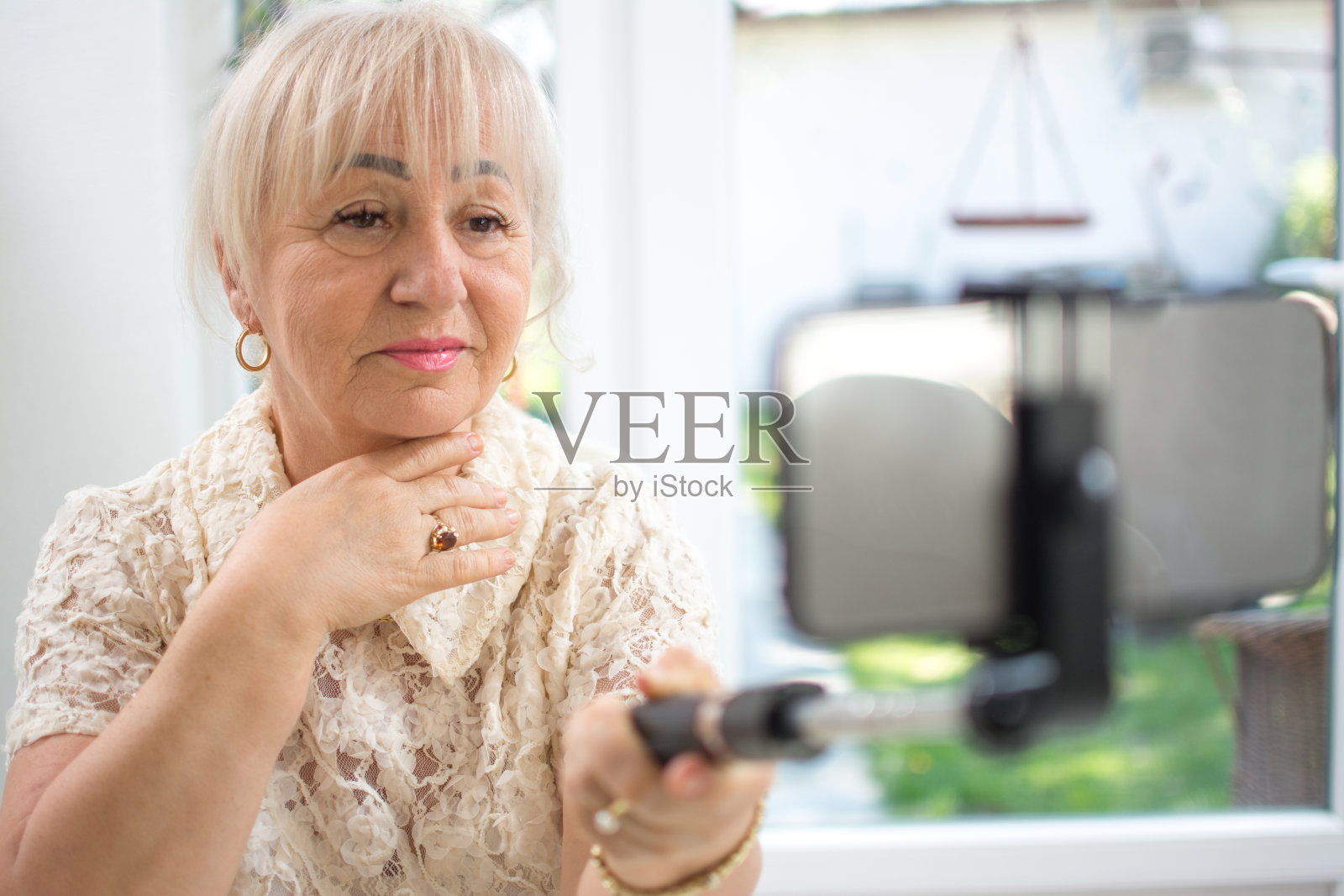 成熟的女人拿着自拍杆和智能手机在家里进行视频通话照片摄影图片