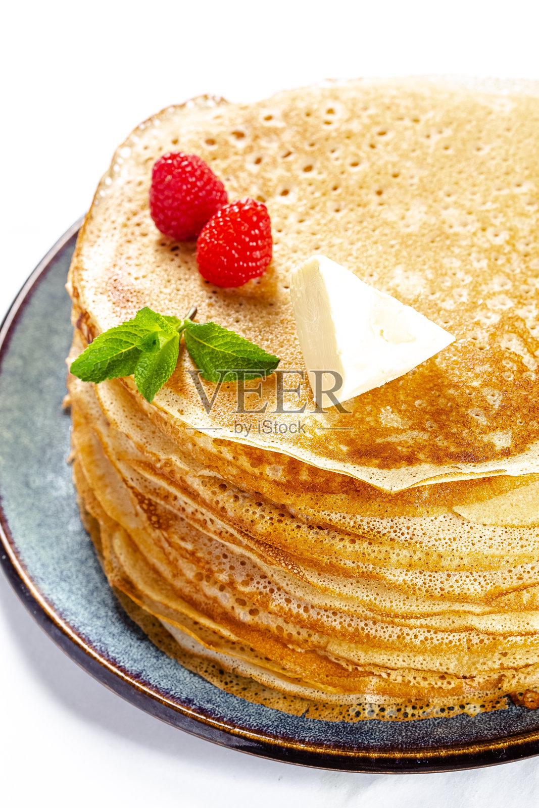 白色孤立的背景，一个盘子和煎饼躺在上面，一块黄油和覆盆子照片摄影图片