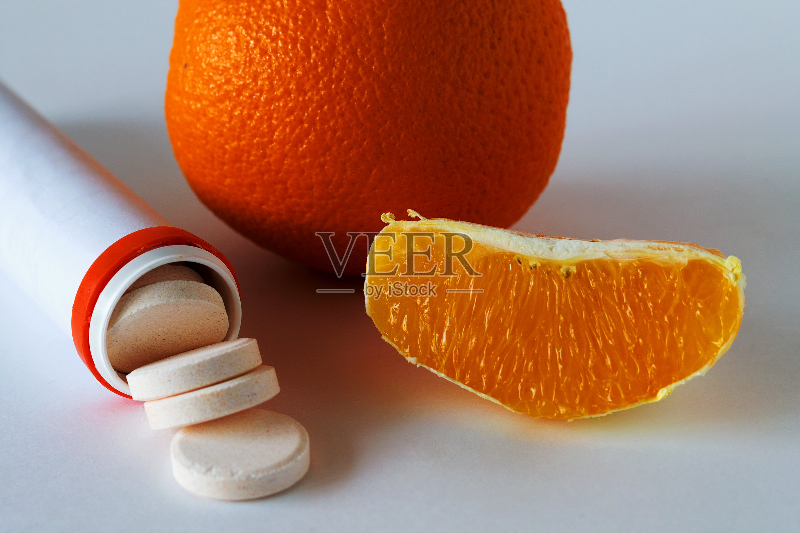 维生素C药片孤立在白色的背景上，新鲜的桔子片在白色的桌子上。装着药丸的橙色药瓶。增强免疫系统。健康的生活方式。柑橘类水果照片摄影图片