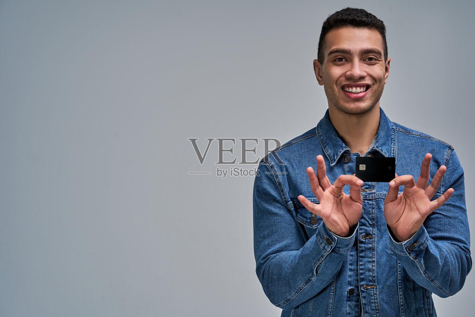 一个穿蓝色夹克的人显示他手里有一张黑色的银行信用卡。银行的概念照片摄影图片