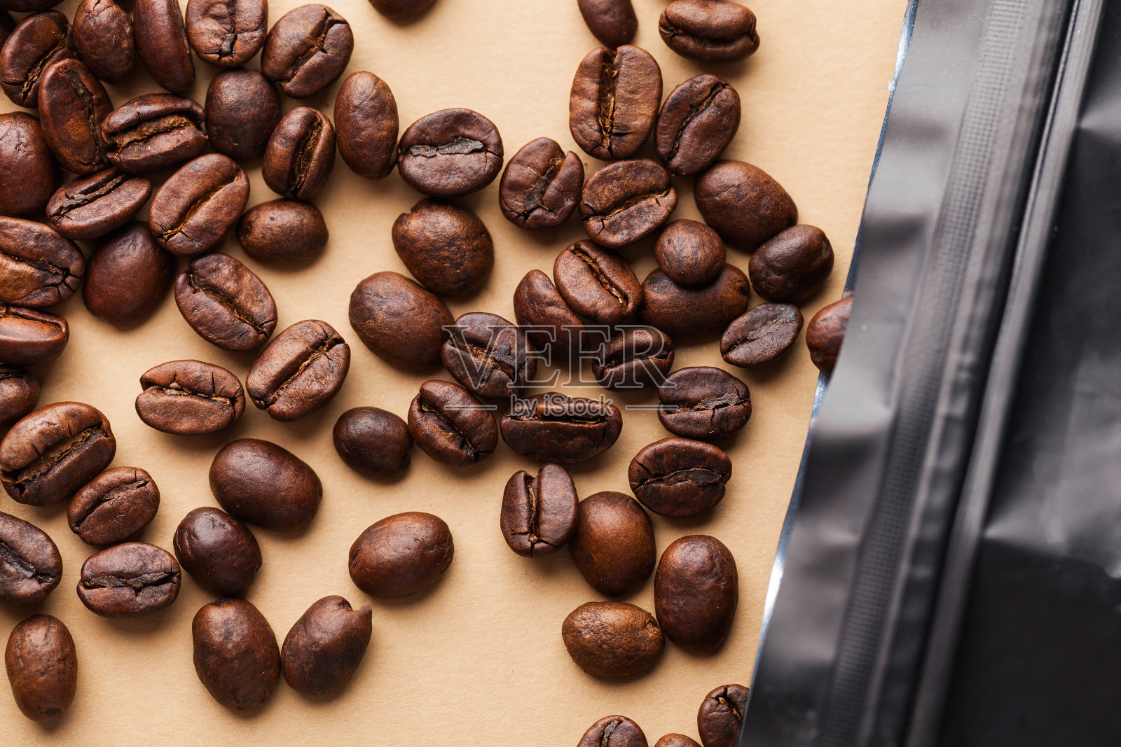 咖啡豆的特写从包装中溢出，在浅棕色的背景上。适合烘焙店、咖啡馆和咖啡店。照片摄影图片