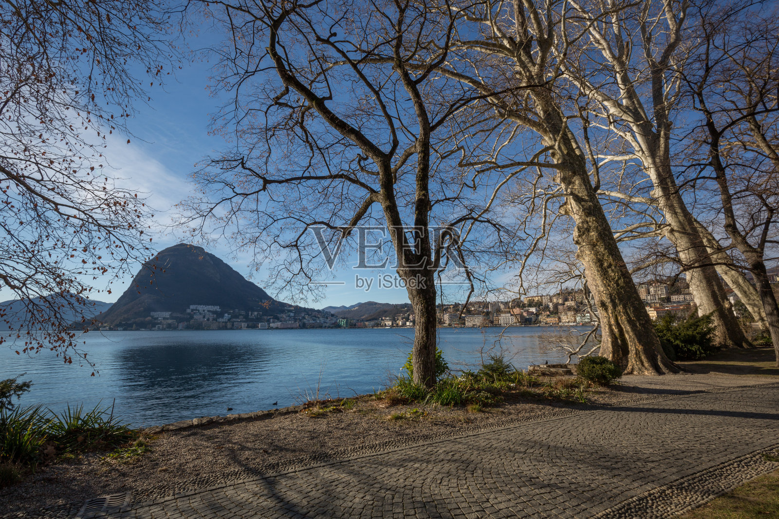 卢加诺湖，远处有薄雾的天空，树木和山脉照片摄影图片