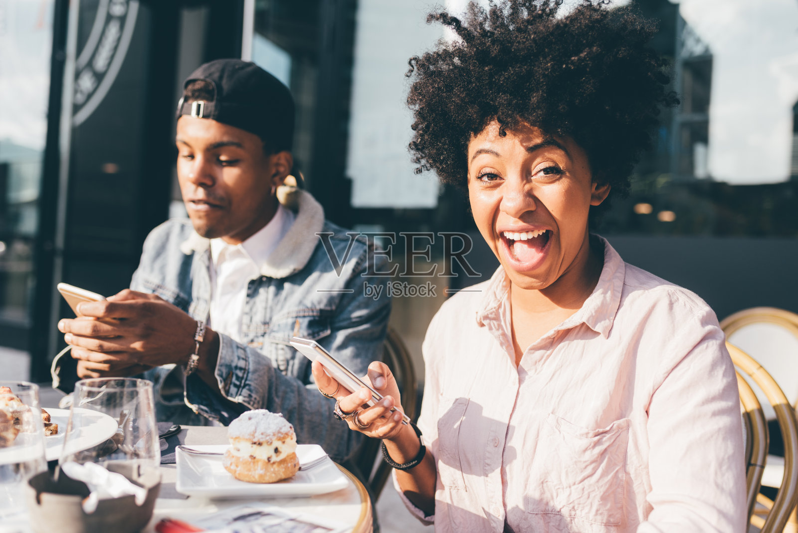 年轻的多民族夫妇正在城市的一个户外酒吧休息，使用智能手机照片摄影图片