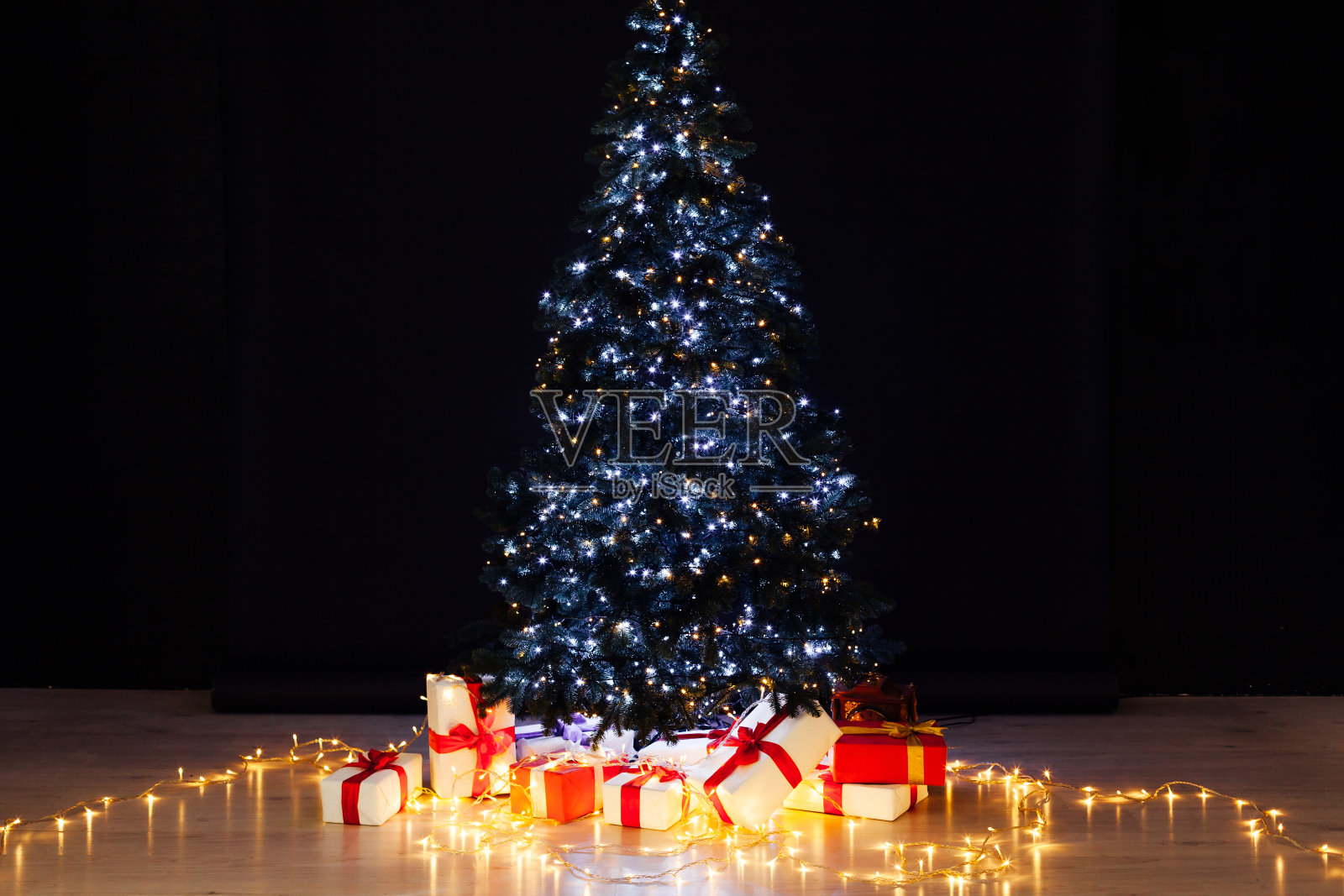 以黑色为背景，装饰着圣诞礼物的圣诞树、彩灯和花环照片摄影图片