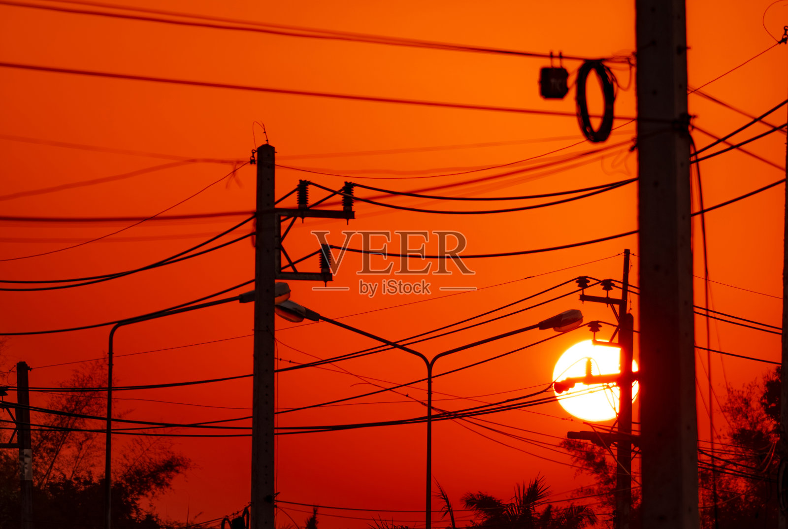 晚上的电线杆和传输线。日落时的电缆塔和路灯柱。农村城市的电力和能源。电线杆后面美丽的红色日落天空。照片摄影图片