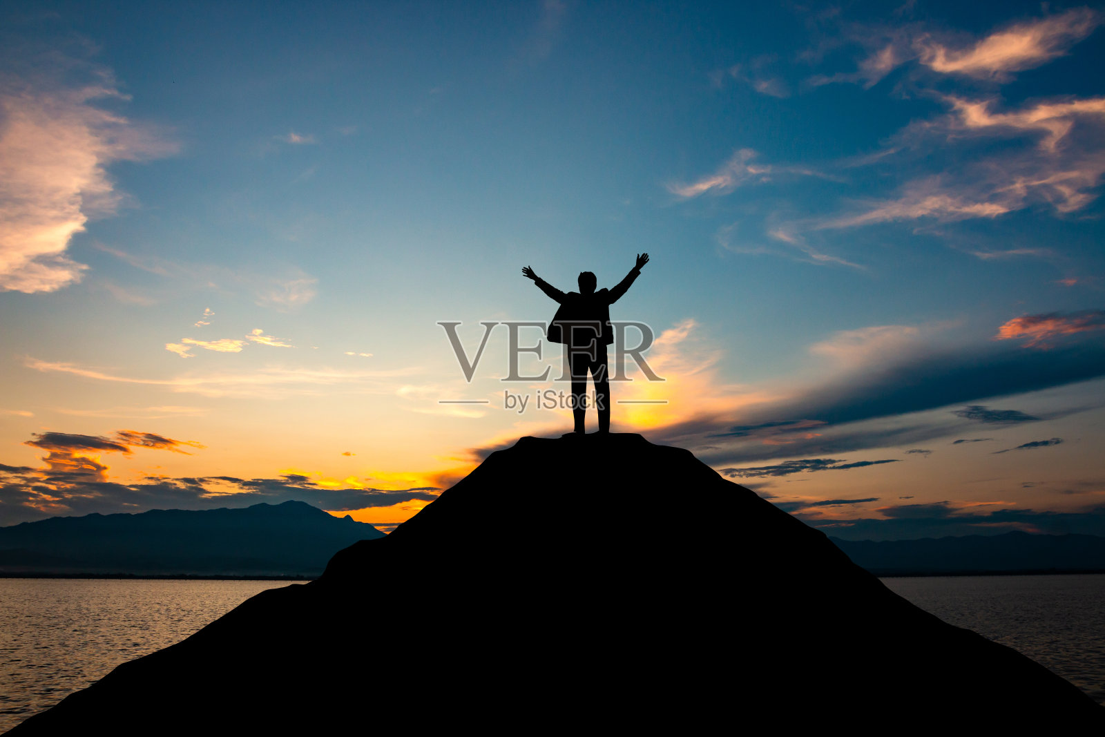 在日落天空的背景下，商人在山顶的剪影，商业，成功，领导和成就的概念照片摄影图片