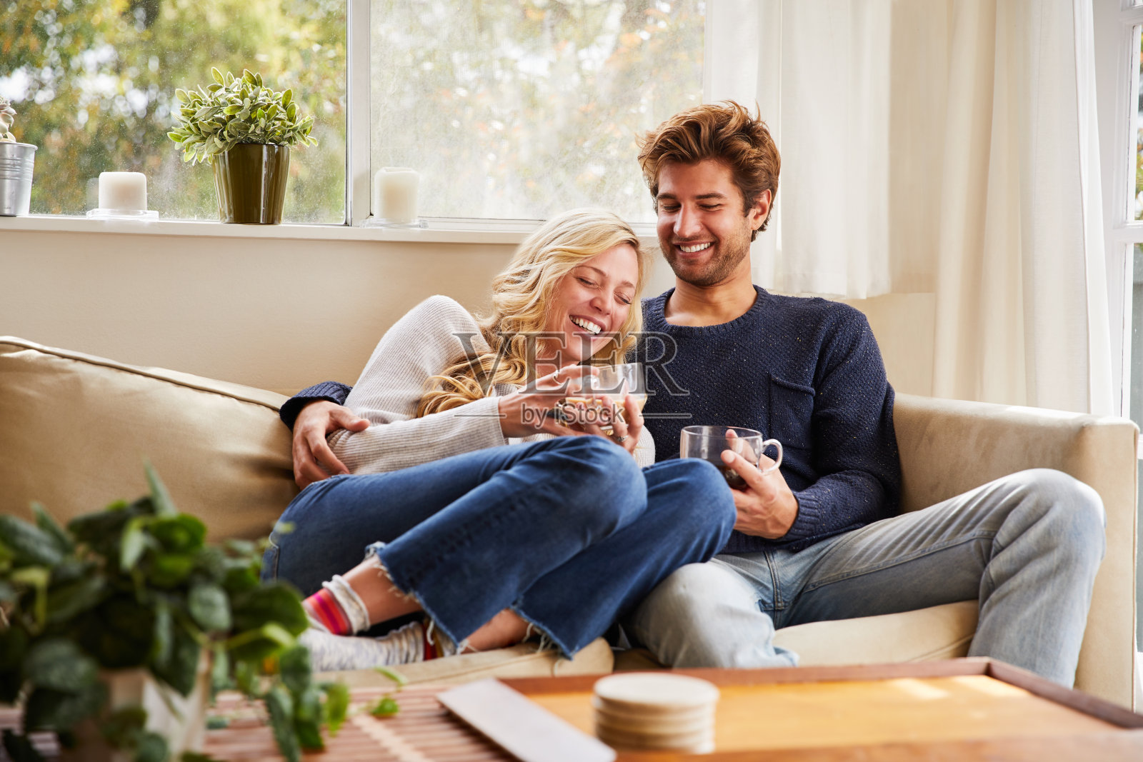 一对年轻夫妇坐在沙发上，边喝咖啡边笑照片摄影图片