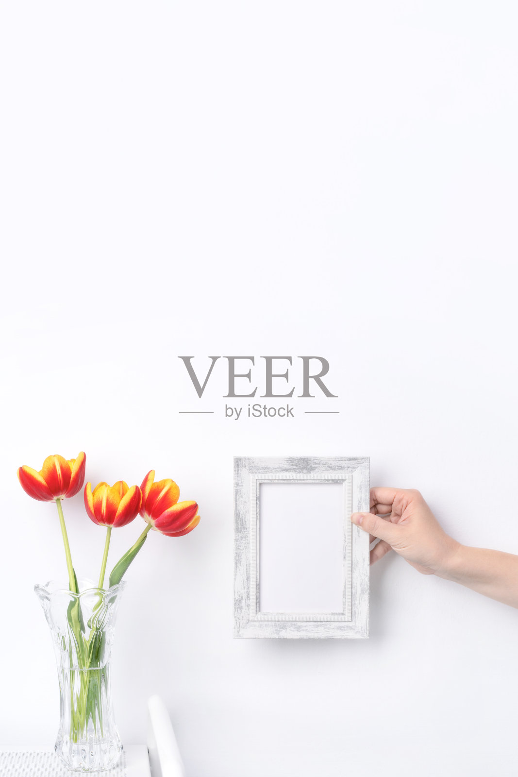 郁金香花在玻璃花瓶与画框放置在白色木桌背景对着干净的墙在家里，近距离，母亲节的装饰概念。照片摄影图片