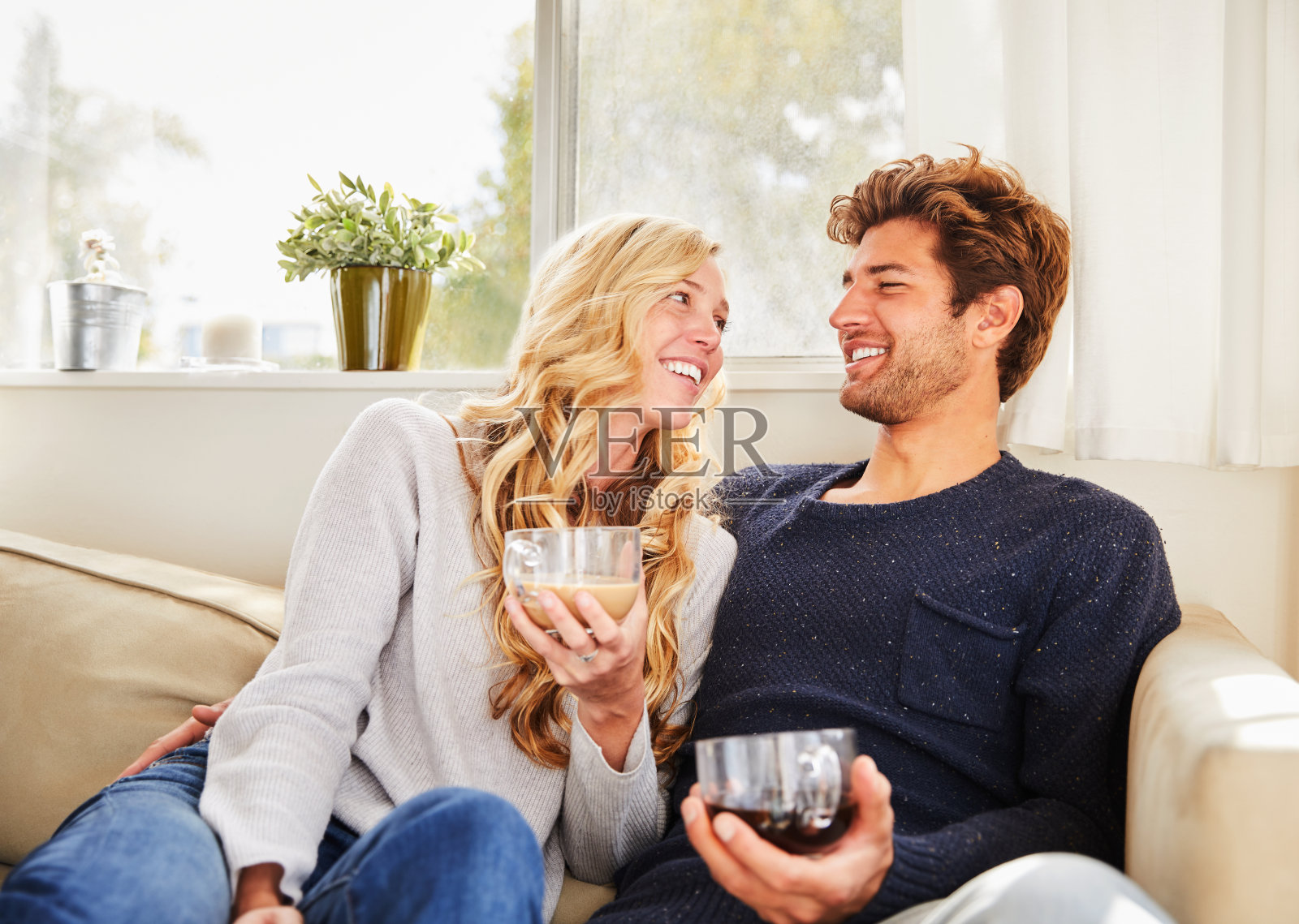 微笑的年轻夫妇在他们的客厅边喝咖啡边聊天照片摄影图片