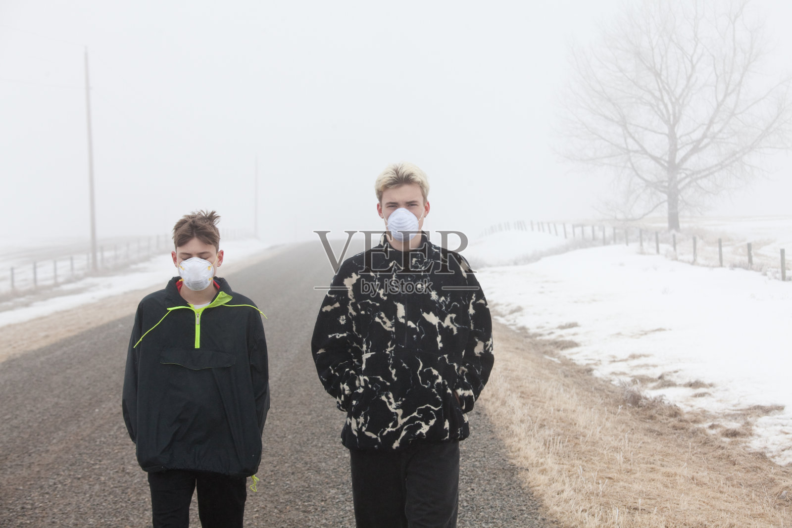 Covid-19大流行期间，两名戴着口罩的白人男孩走在雾蒙蒙的乡村道路上照片摄影图片