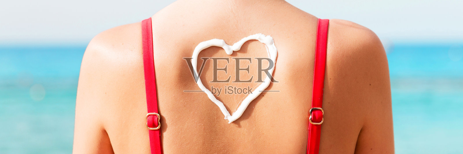 穿着红色泳衣的美丽女孩在海滩背部涂有心形防晒霜照片摄影图片