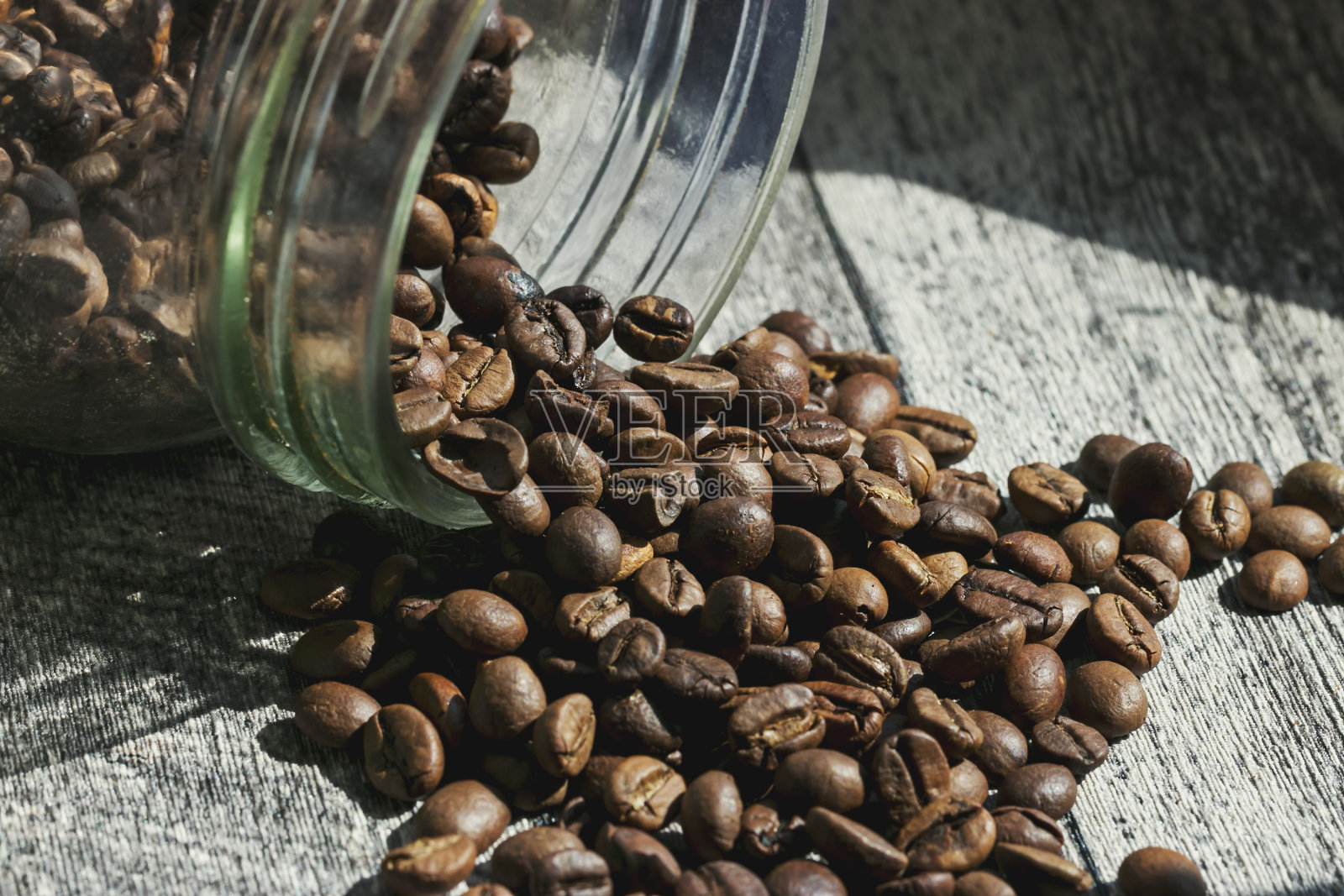 桌上放着一罐咖啡，咖啡豆撒得到处都是。照片摄影图片