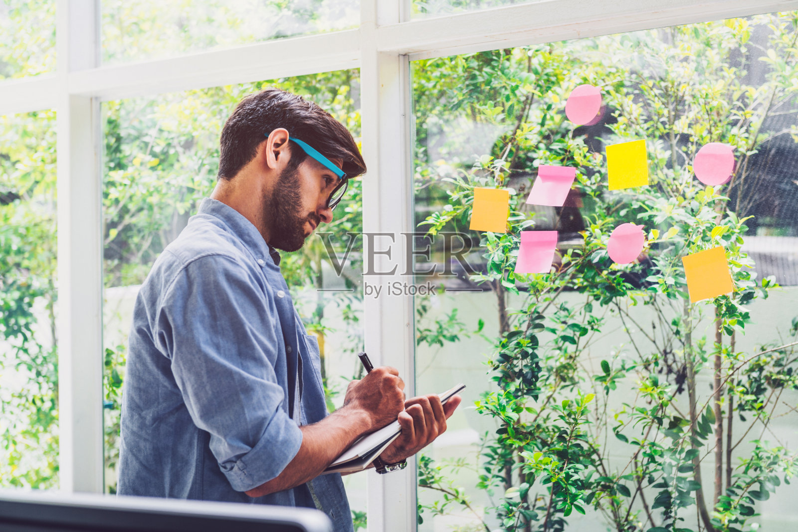 一个年轻人一边在办公室里看便利贴，一边在书上写字照片摄影图片