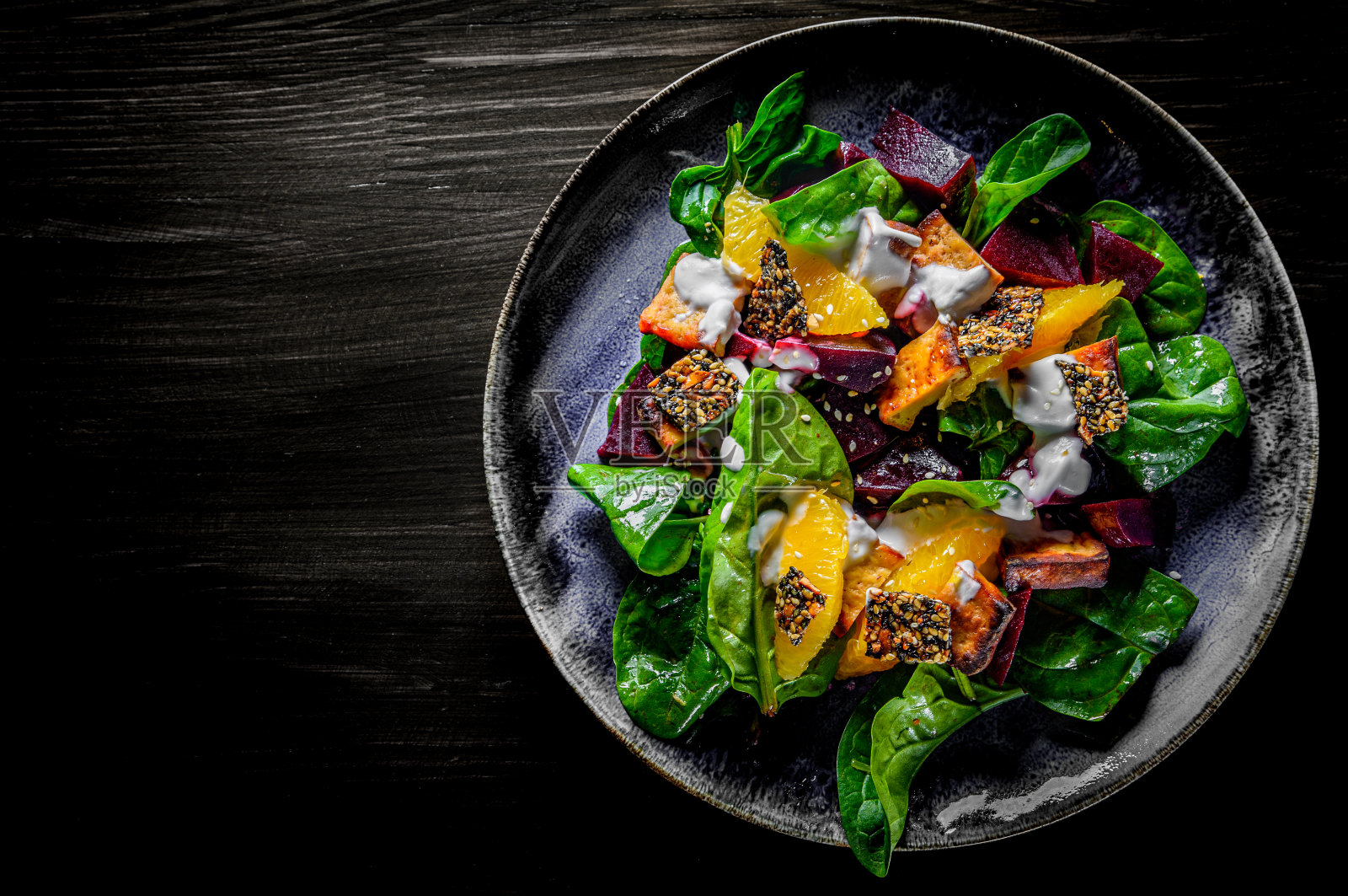 蔬菜沙拉配甜菜，菠菜，橙子，豆腐在盘子里的黑色木制桌子背景照片摄影图片