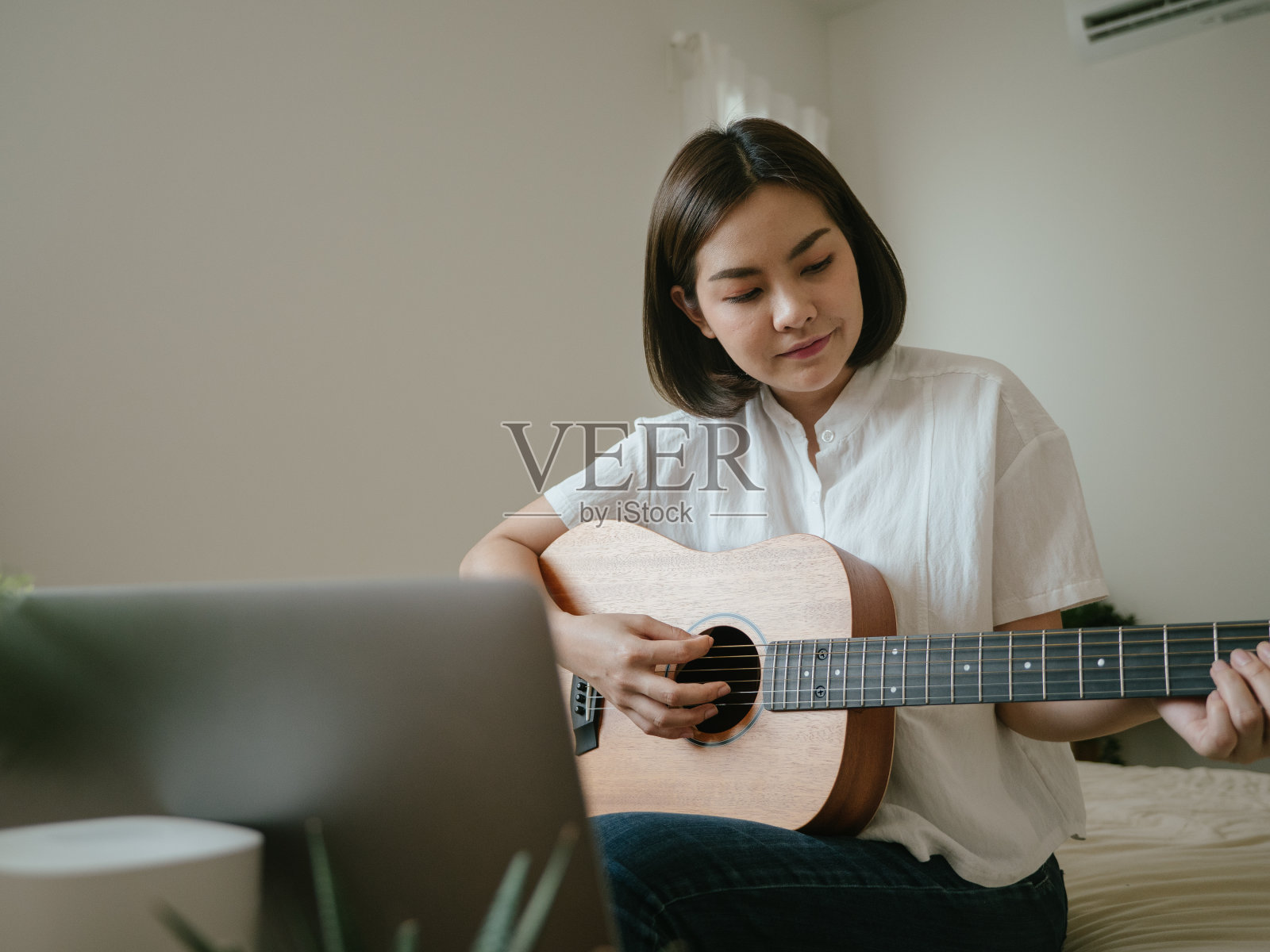 年轻女子一边玩原声吉他一边用笔记本电脑视频聊天照片摄影图片