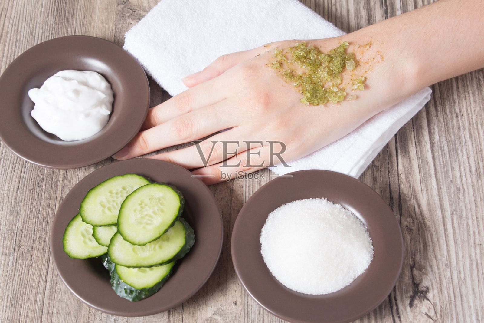 皮肤护理在家。一位妇女将自制的天然磨砂膏涂在手上。磨砂膏的配料，盐，糖，黄瓜，奶油。保湿、去角质、去角质、SPA、美容院。生态照片摄影图片