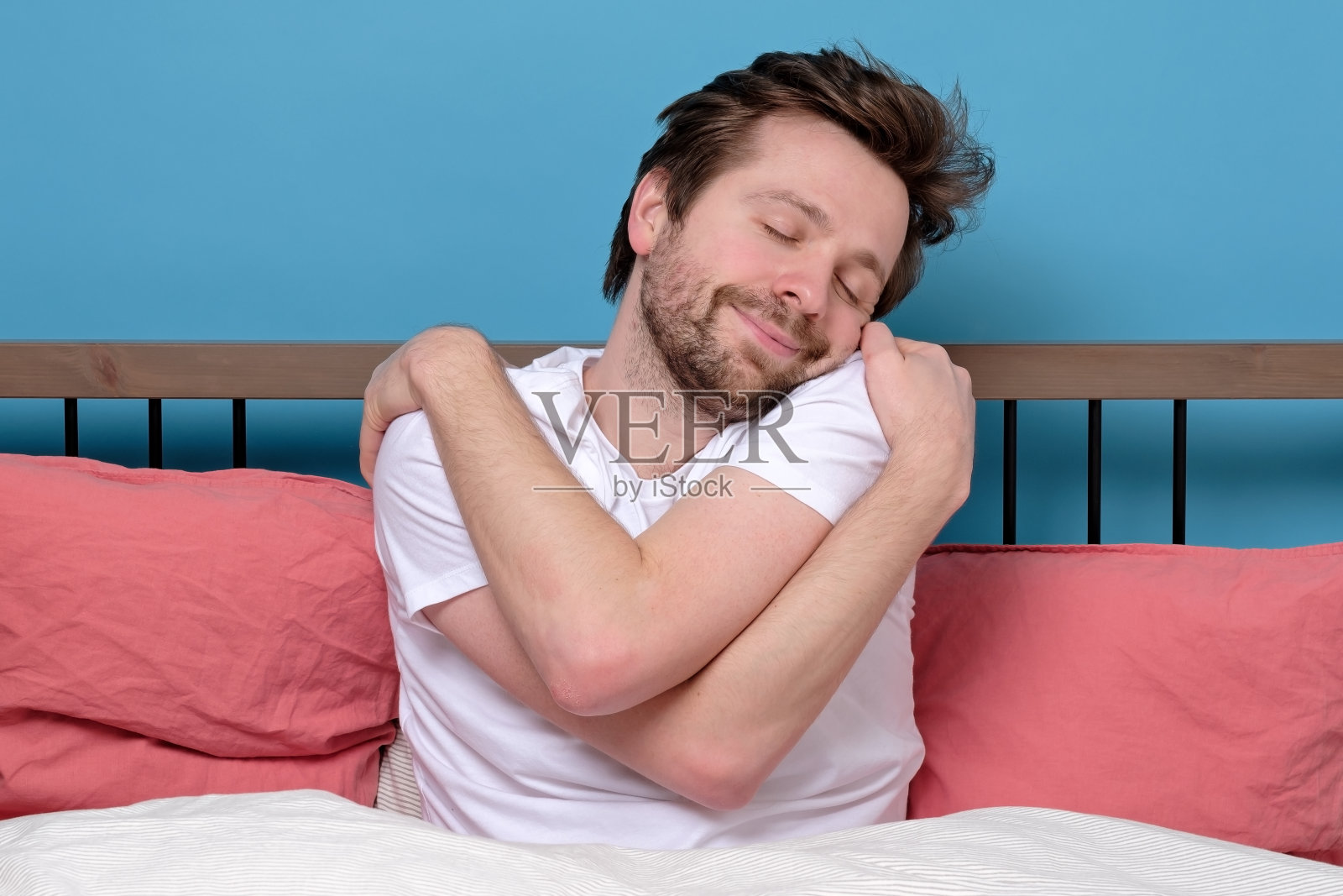 成熟的白种男人独自在床上闭着眼睛拥抱自己。照片摄影图片