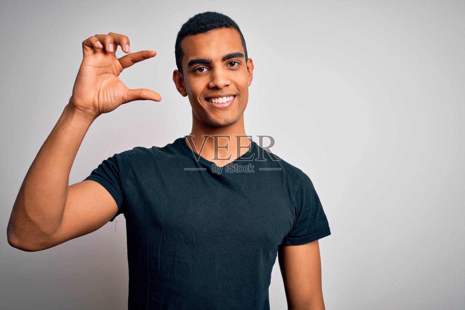 年轻英俊的非裔美国人穿着休闲t恤站在白色背景微笑和自信的手势与手做小尺寸的标志与手指看和相机。测量的概念。照片摄影图片